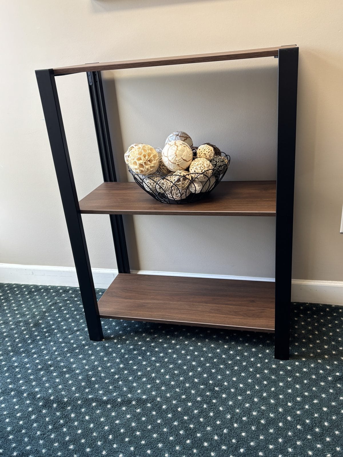 UPLIFT Sequence Shelving short unit in black powder-coated steel with walnut shelves, holding a decorative bowl of dried spheres against the reception room wall.