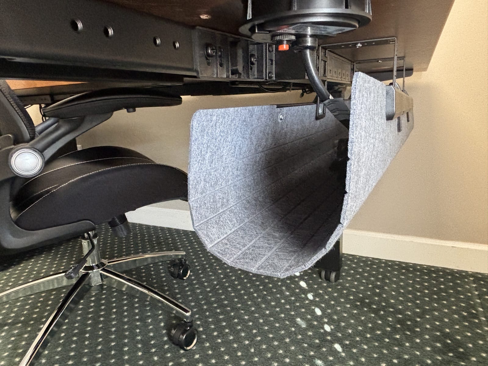 Underside of the reception desk showing the frame and the gray felt FlexMount Cable Manager basket holding power cords beneath the desktop, with an office chair nearby.