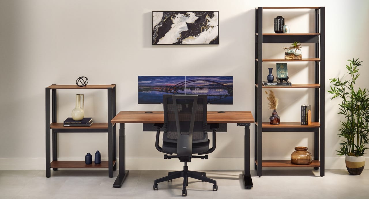 UPLIFT product photo of a short Sequence Shelving unit and a tall Sequence Shelving unit, both with black frames and wood-tone shelves, on either side of a standing desk.